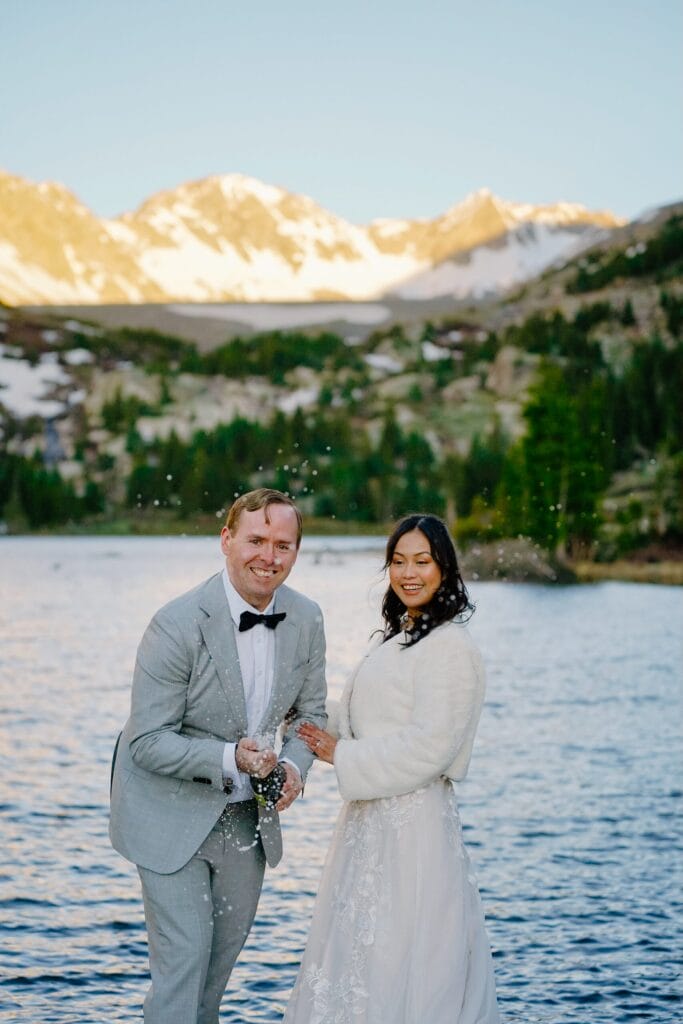 groom spraying champagne at the camera while the bride smiles at him after their self-solemnization ceremony during their breckenridge elopement in colorado