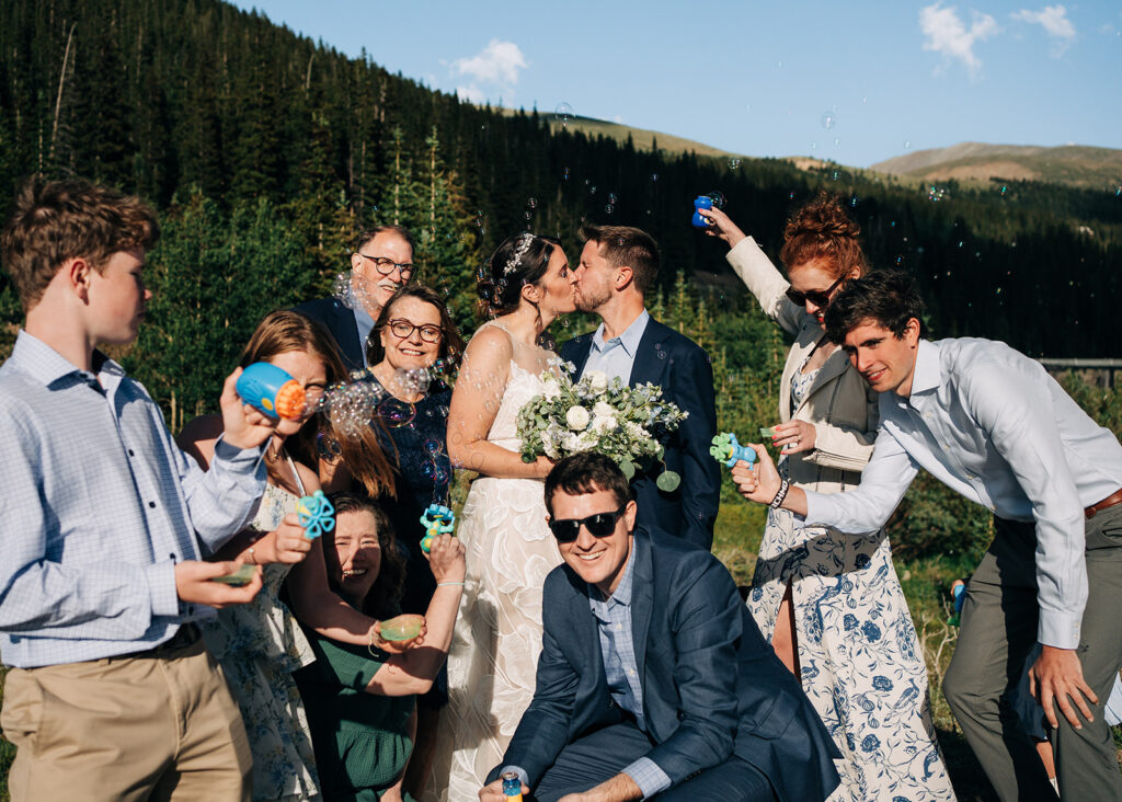 bride and groom kissing while family celebrates around them during their new mexico elopement
