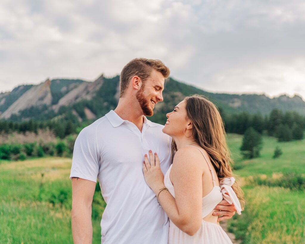 girlfriend looking up at her boyfriend with a smile with the boulder colorado flatirons in the background during their couples photoshoot at chautauqua park
