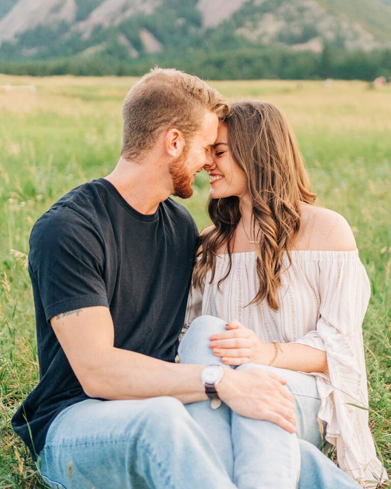 couple sitting together cuddled up in the grassy with their foreheads pressed together during their boulder colorado engagement session at chautauqua park
