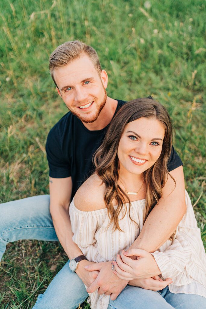 cute couples sitting in the grass smiling up at the camera during their boulder colorado couples session at chautauqua park