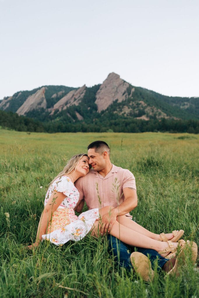 Couple sitting in grassy field with mountains background.