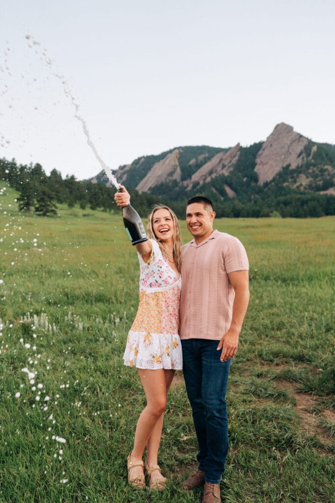 Couple celebrating with champagne in scenic field.