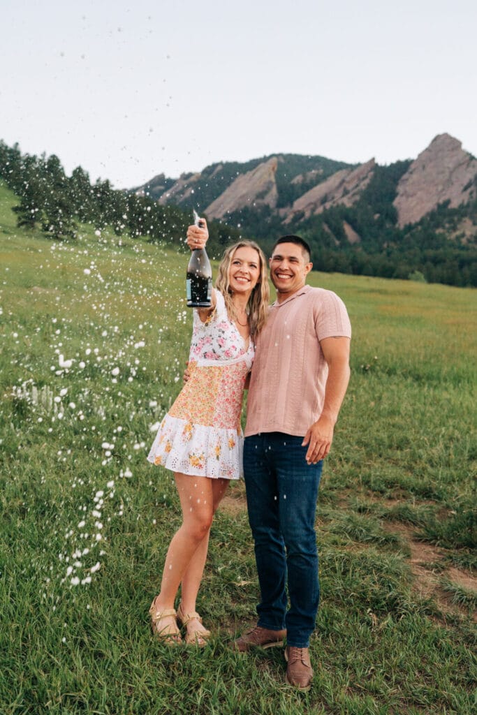 Couple celebrating with champagne in scenic landscape.