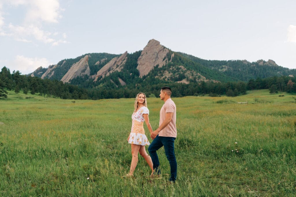 Couple holding hands in grassy mountain landscape.