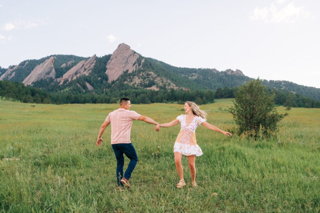 Couple holding hands, dancing in grassy field.