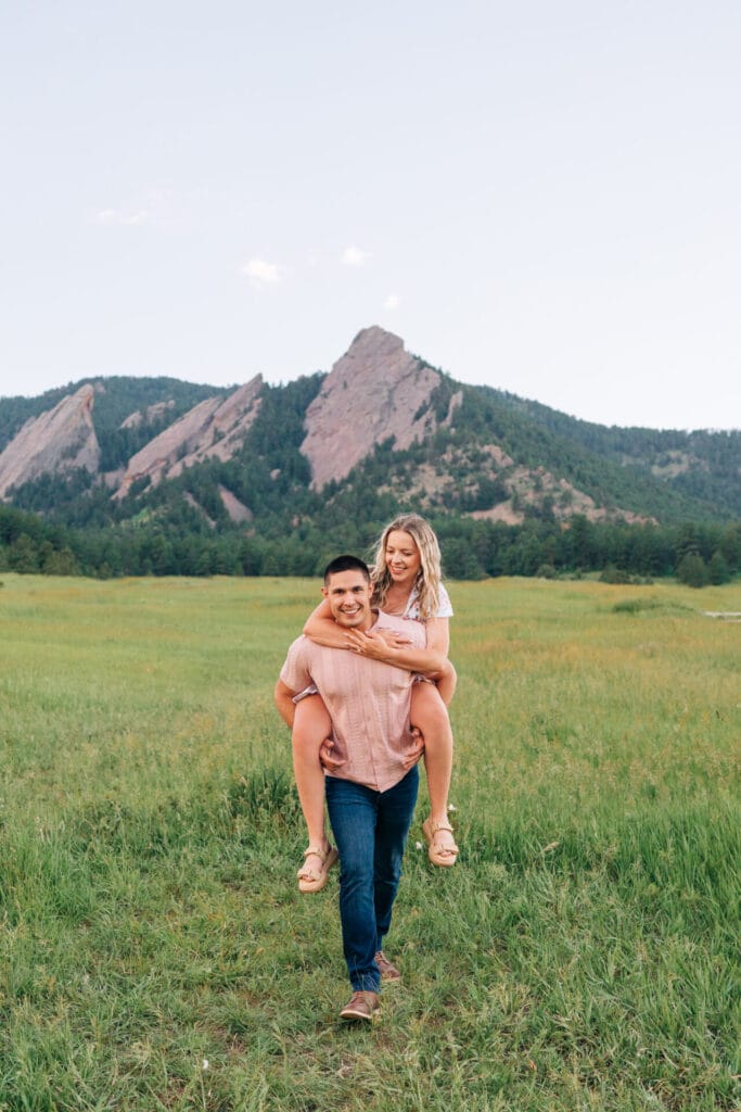Couple enjoying piggyback ride in scenic mountain meadow.