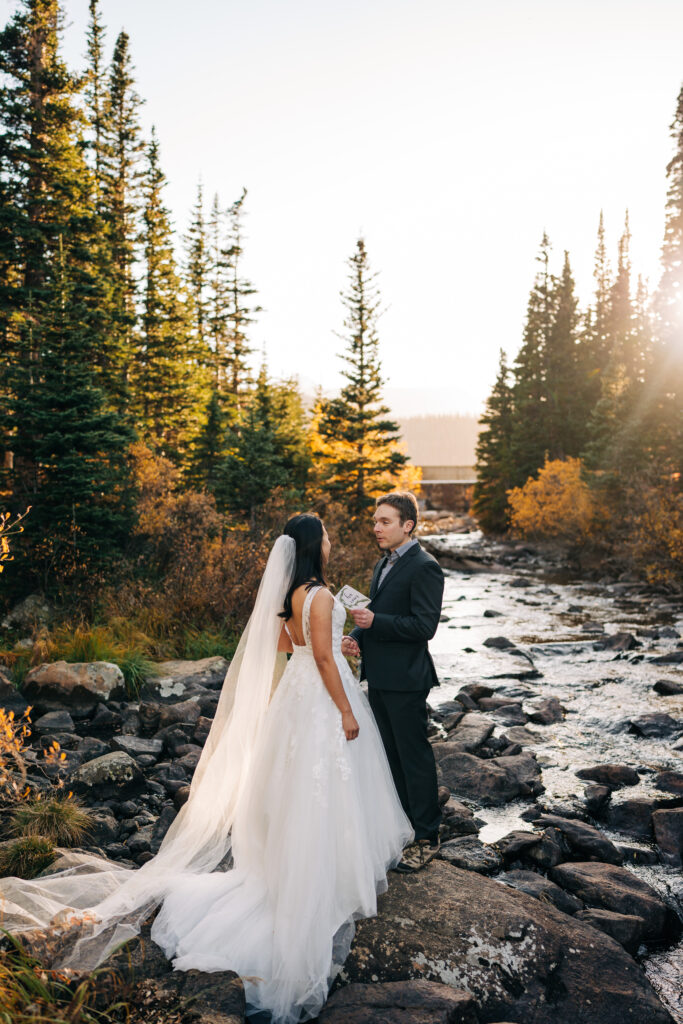 groom reading vows to his bride next to a rocky river during there lake brainard elopement in colorado