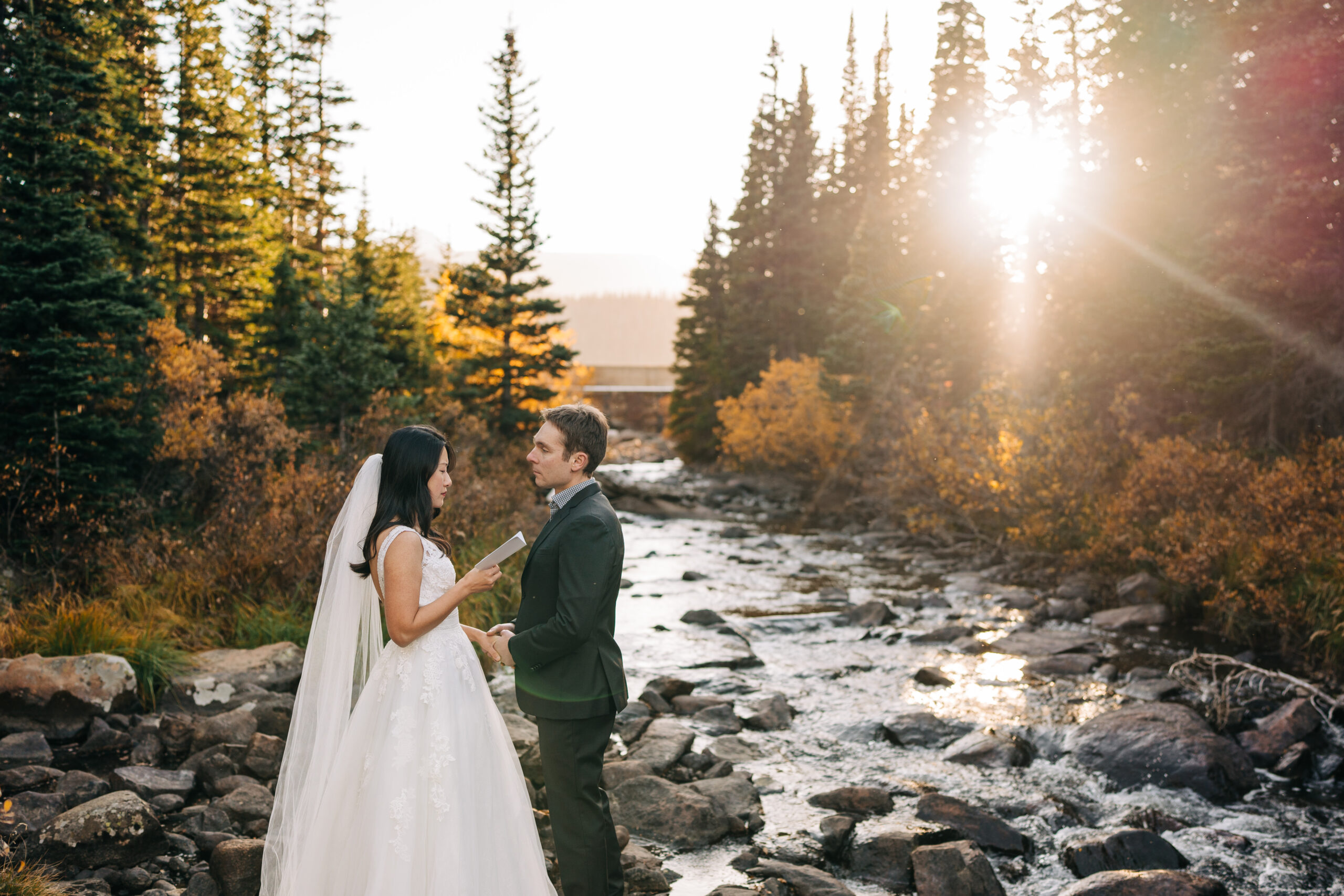 a beautiful fall sunset in colorado where a bride is reading her marriage vows to the groom while standing next to a rocky river during their brainard lake elopement