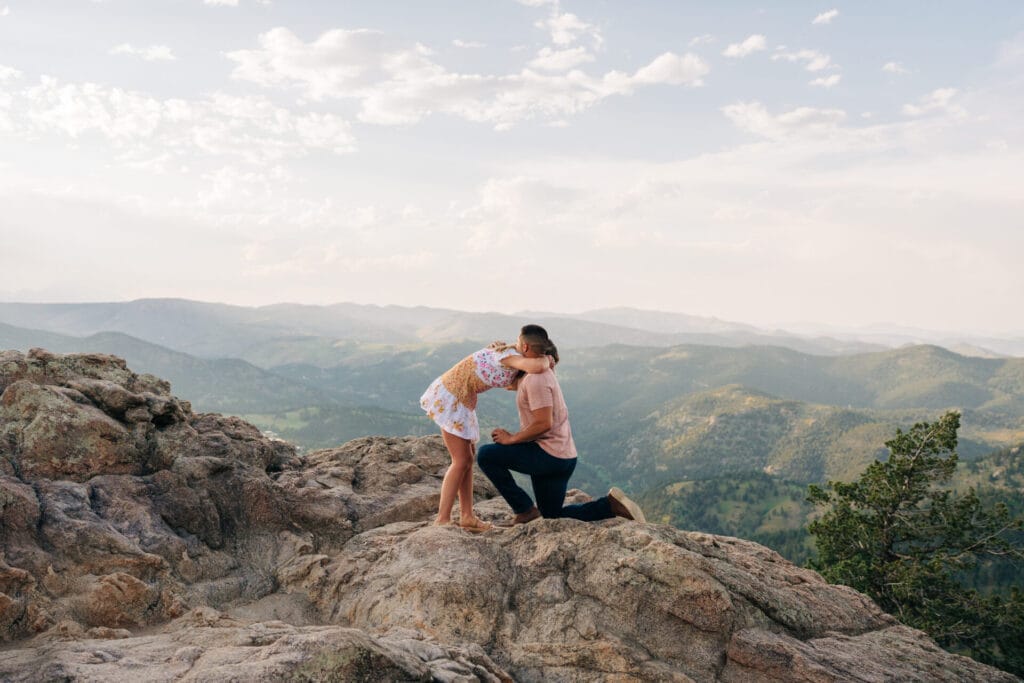 Girlfriend hugging boyfriend as he proposes to her on a cliff at sunset at Lost gulch overlook in Boulder, Colorado