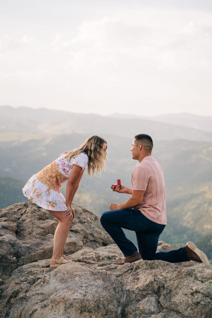 Girl leaning over as her boyfriend proposes on a cliff at Lost Gulch Overlook in Boulder, Colorado