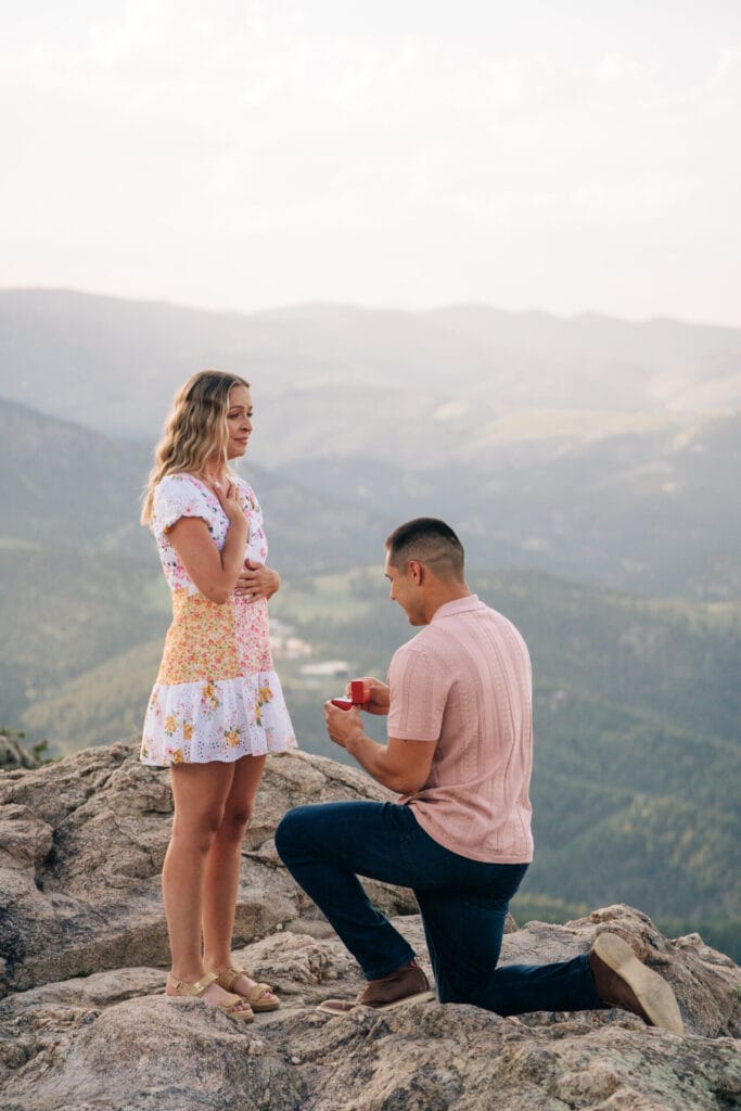 Girlfriend holding her chest during her boyfriend proposing on cliff at Lost Gulch Overlook in Boulder, Colorado