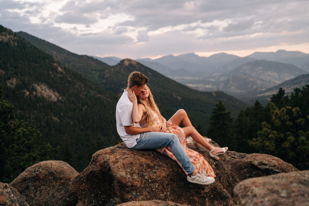 engaged couple sitting on a rocky outcropping at rocky mountain national park during their lily lake engagement photos