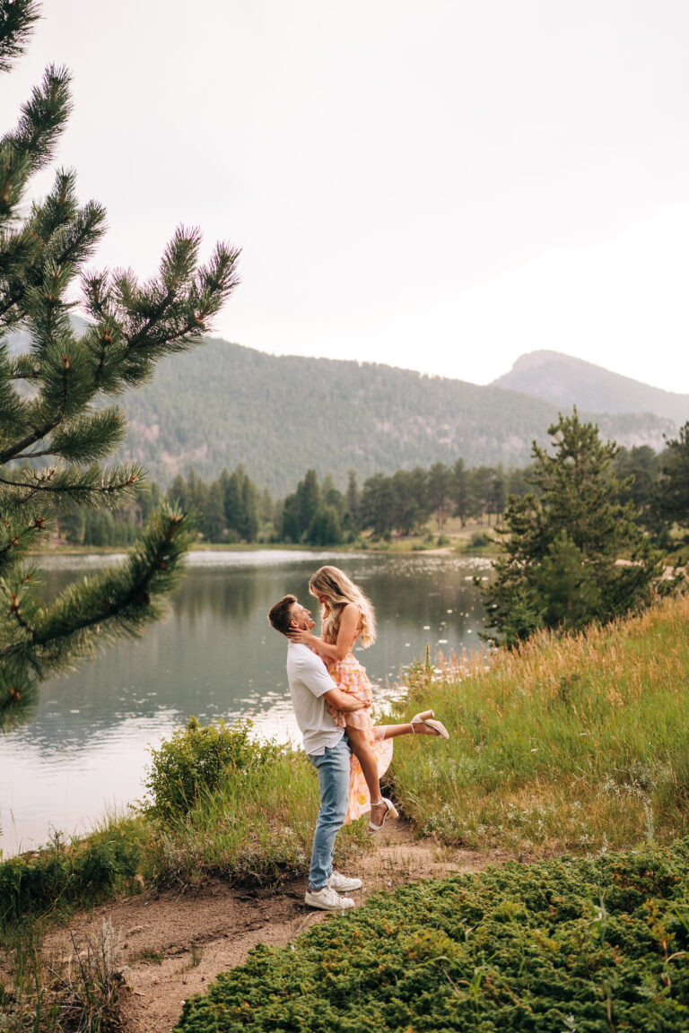 boyfriend picking his girlfriend up on the lakeshore during their lily lake engagement photos in rocky mountain national park near estes park