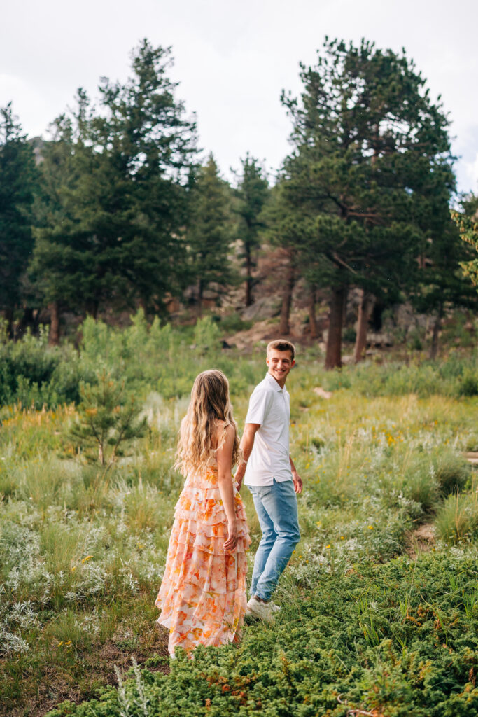 boyfriend leading his girlfriend through a meadow during their lily lake engagement photos