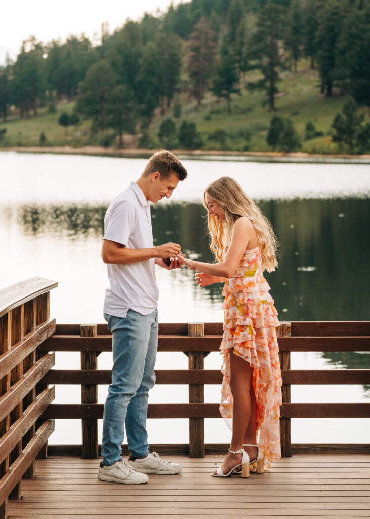 boyfriend placing engagement ring on his girlfriends finger during their lily lake engagement photos