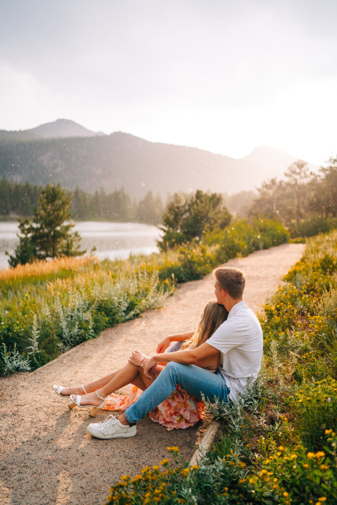 boyfriend hugging his girlfriend from behind as they sit on a path during their lily lake engagement photos