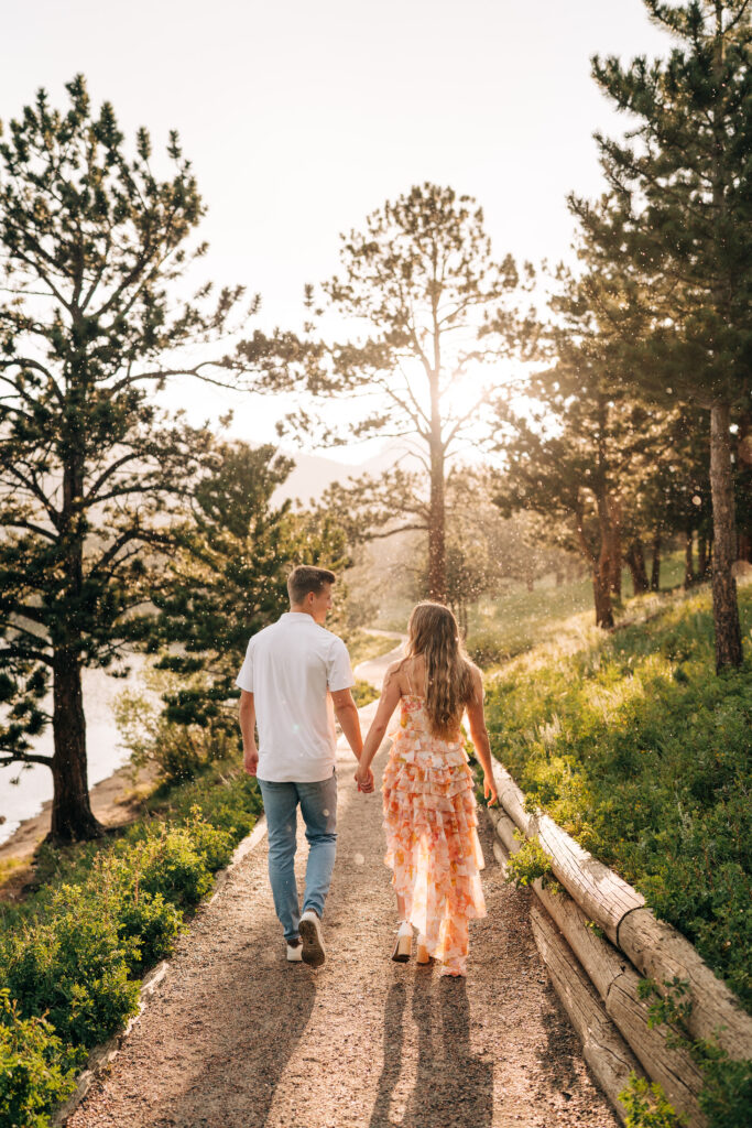 engaged couple holding hands and walking down a trail in the rain during their lily lake engagement photos near estes park