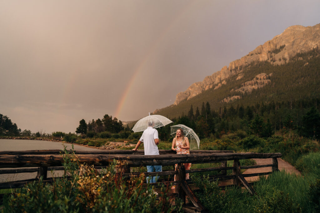 couple standing on a bridge together in the rain during their engagement photos at lily lake in estes park