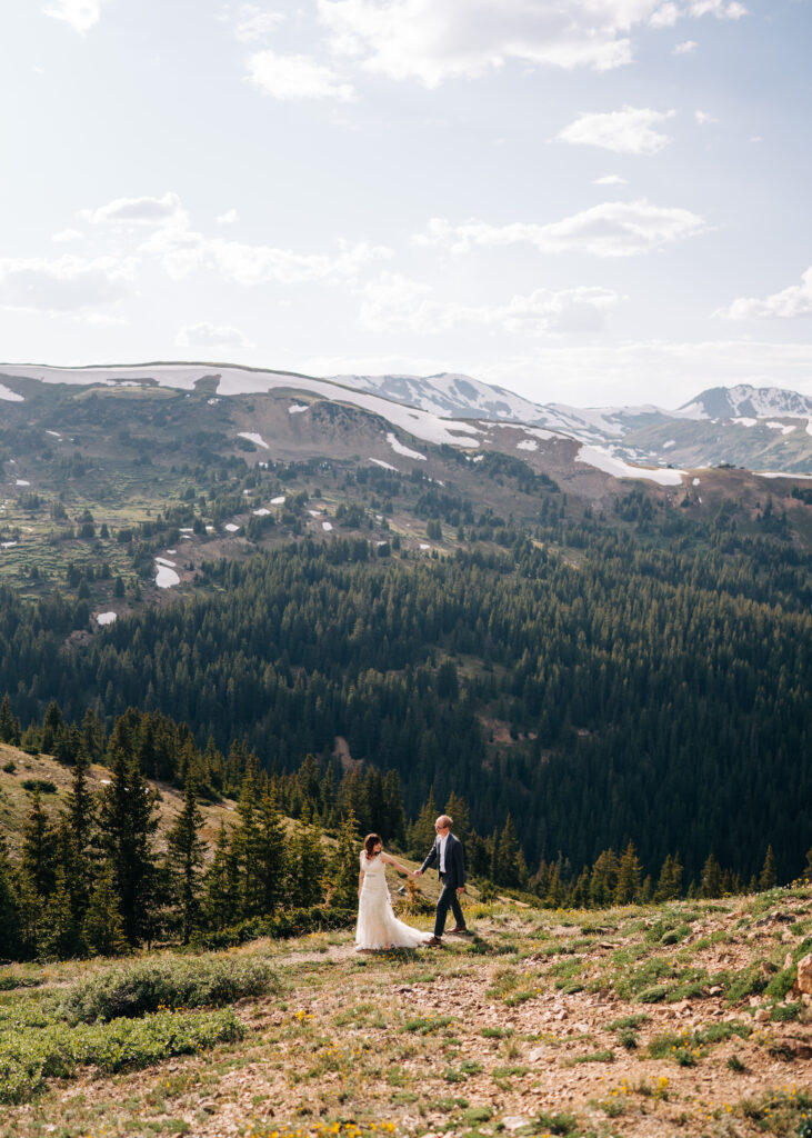 bride and groom holding hands walking down a path during their loveland pass elopement