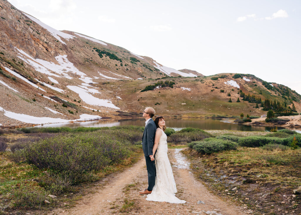 bride and groom standing back to back in front of an alpine lake during their loveland pass elopement