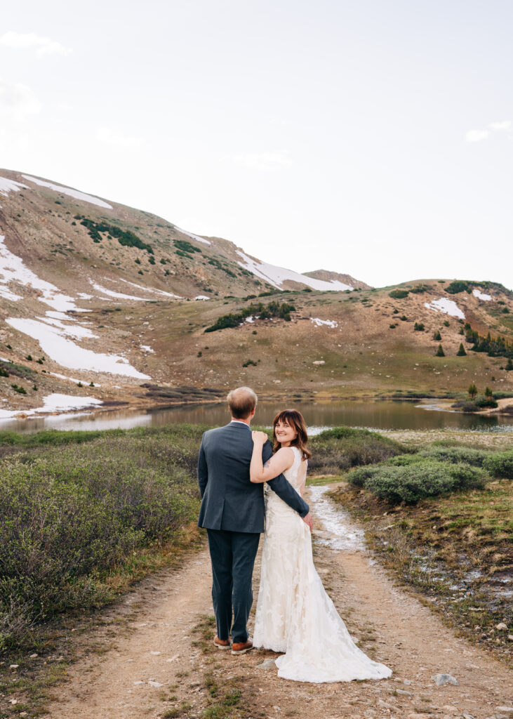 bride and groom walking away from the camera while bride looks back and smiles during their loveland pass elopement