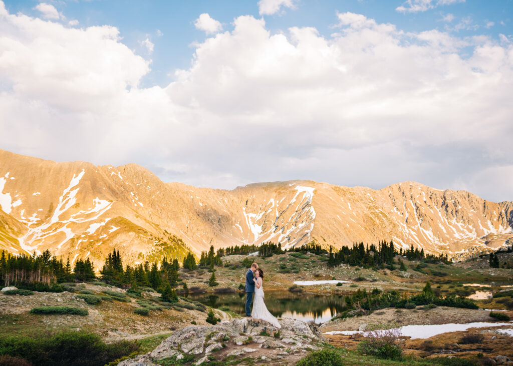 bride and groom standing on a rocky outcropping above a lake during their loveland pass elopement