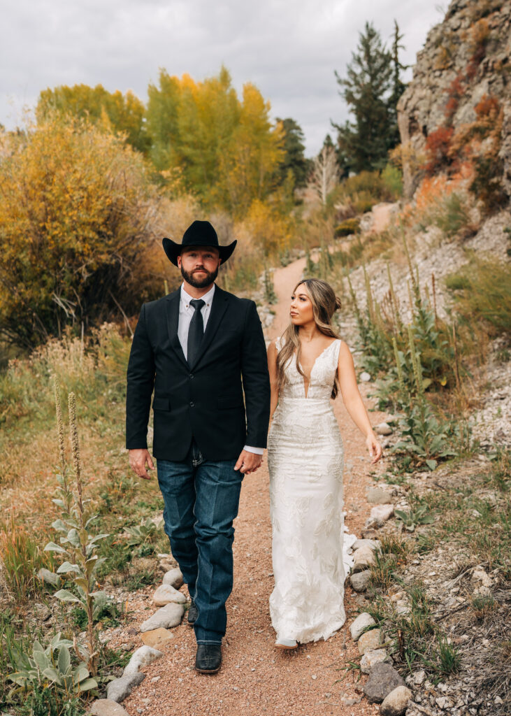 bride and groom holding hands and walking down a path together during their lake city colorado elopement
