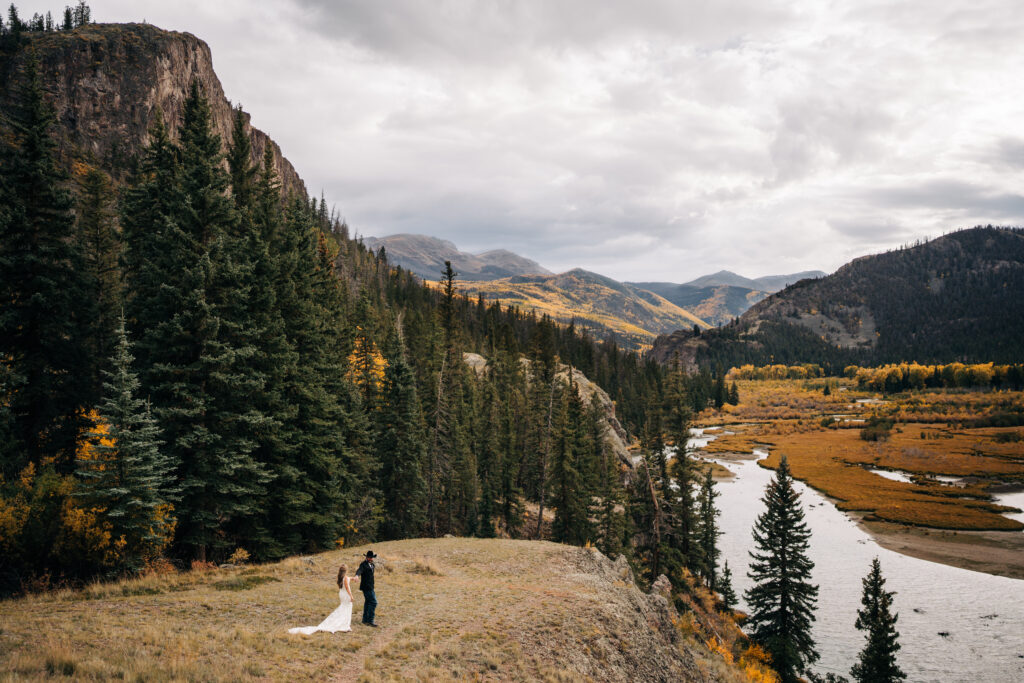 bride and groom walking together with mountains and a lake in the background during their lake city colorado elopement