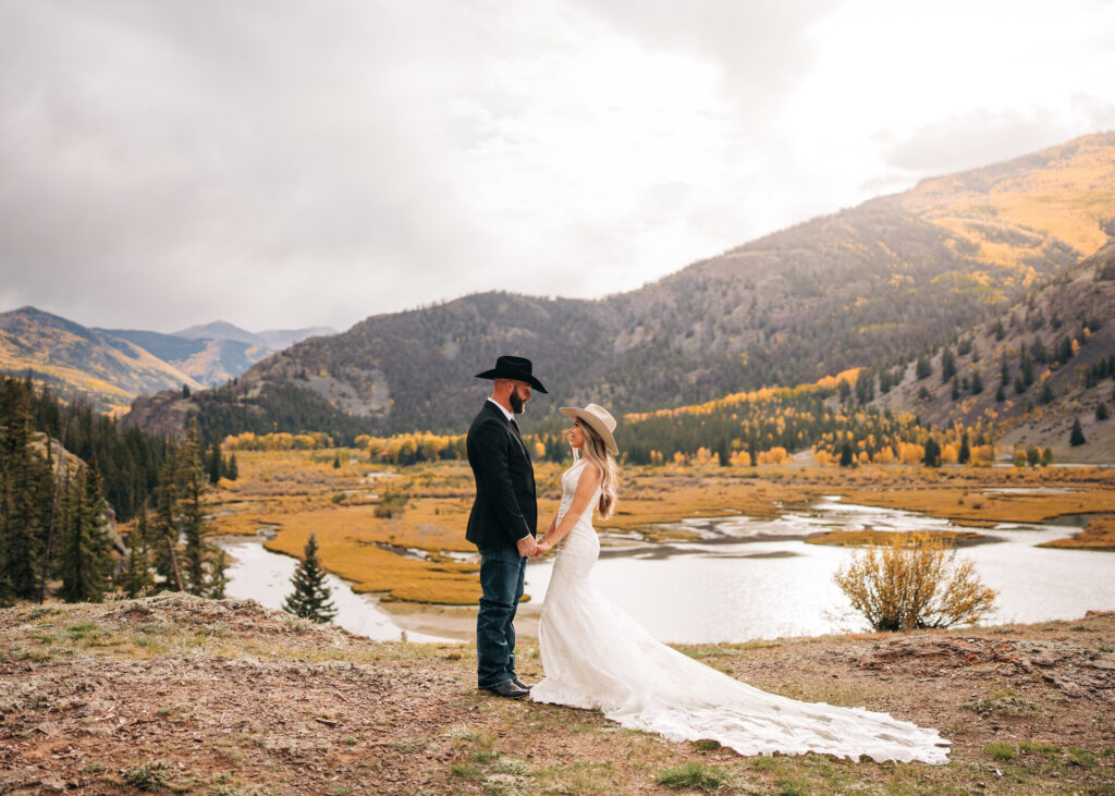 bride and groom holding hands during sunset photos on a cliff with a lake in the background during their lake city colorado elopement