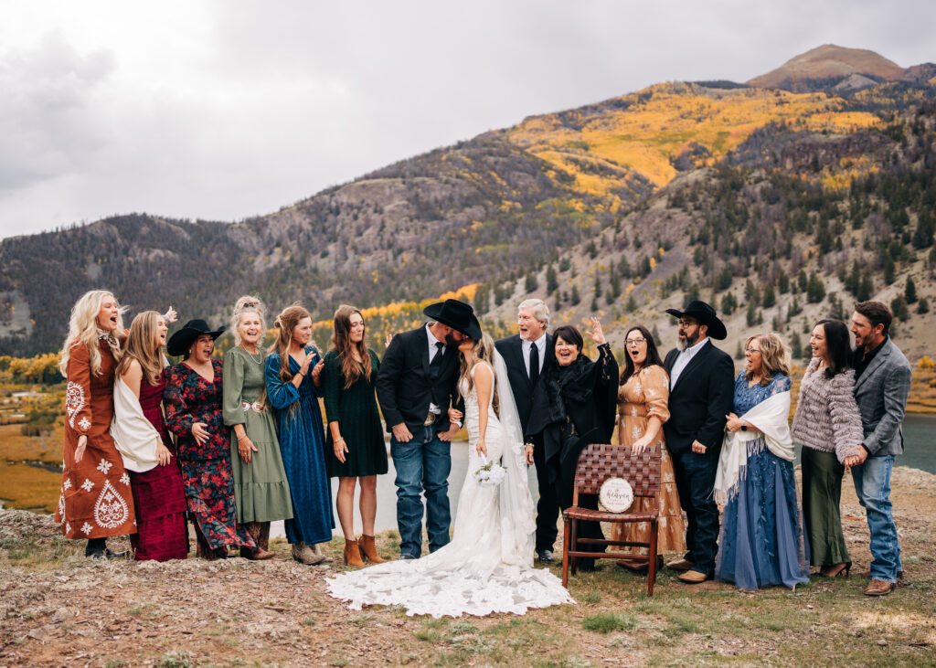 bride and groom kissing while family cheers during their lake city colorado elopement