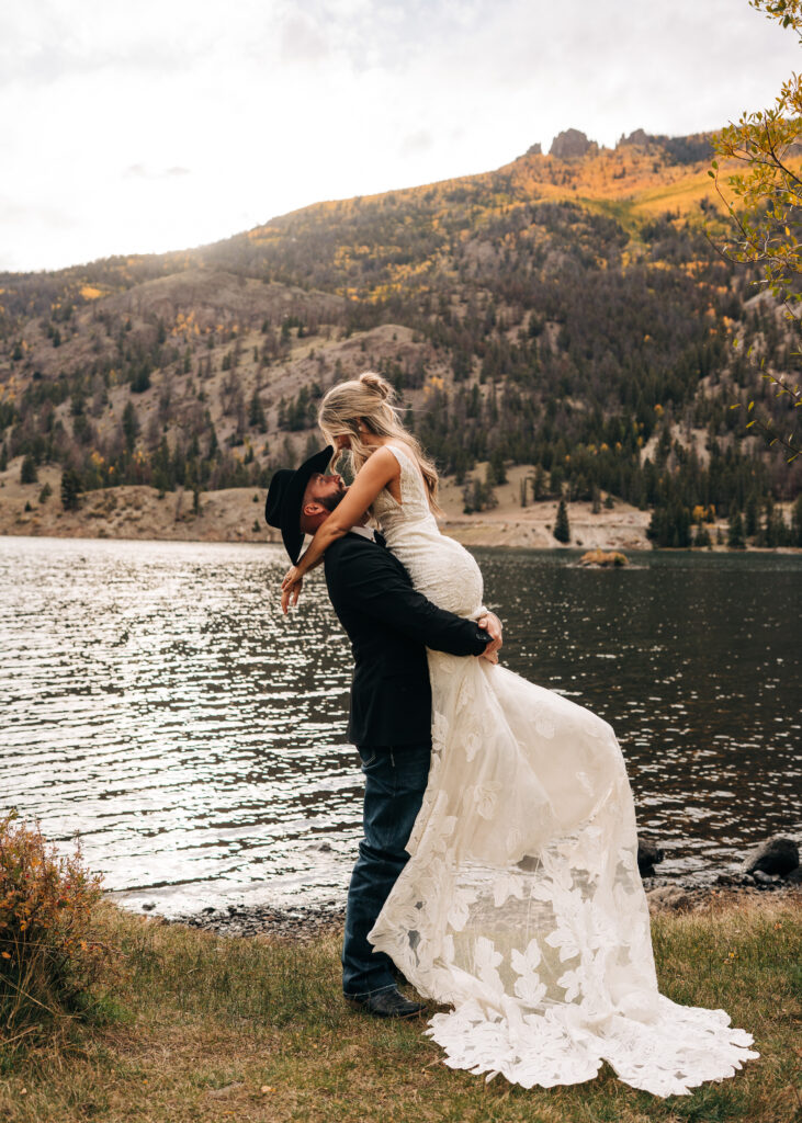 groom picking bride up next to Lake San Cristobal during their bride and groom portraits at their lake city colorado elopement