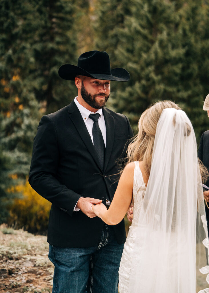 groom holding brides hands smiling down at her during their lake city colorado elopement ceremony