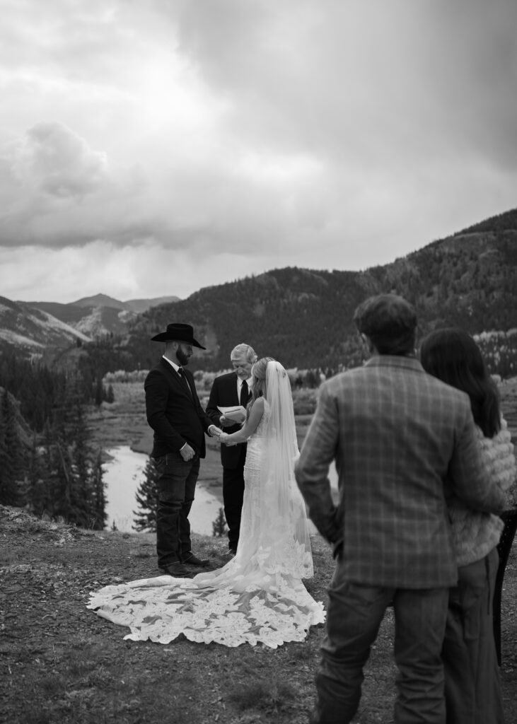 black and white image of bride and groom holding hands during their elopement ceremony on a cliff in lake city colorado