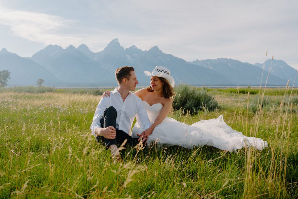 bride and groom sitting in a field in front of the grand tetons during their elopement