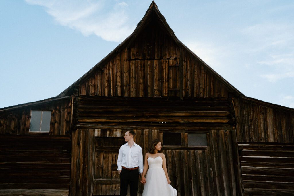 bride and groom holding hands in front of a barn on mormon row during couples grand teton national park elopement portraits