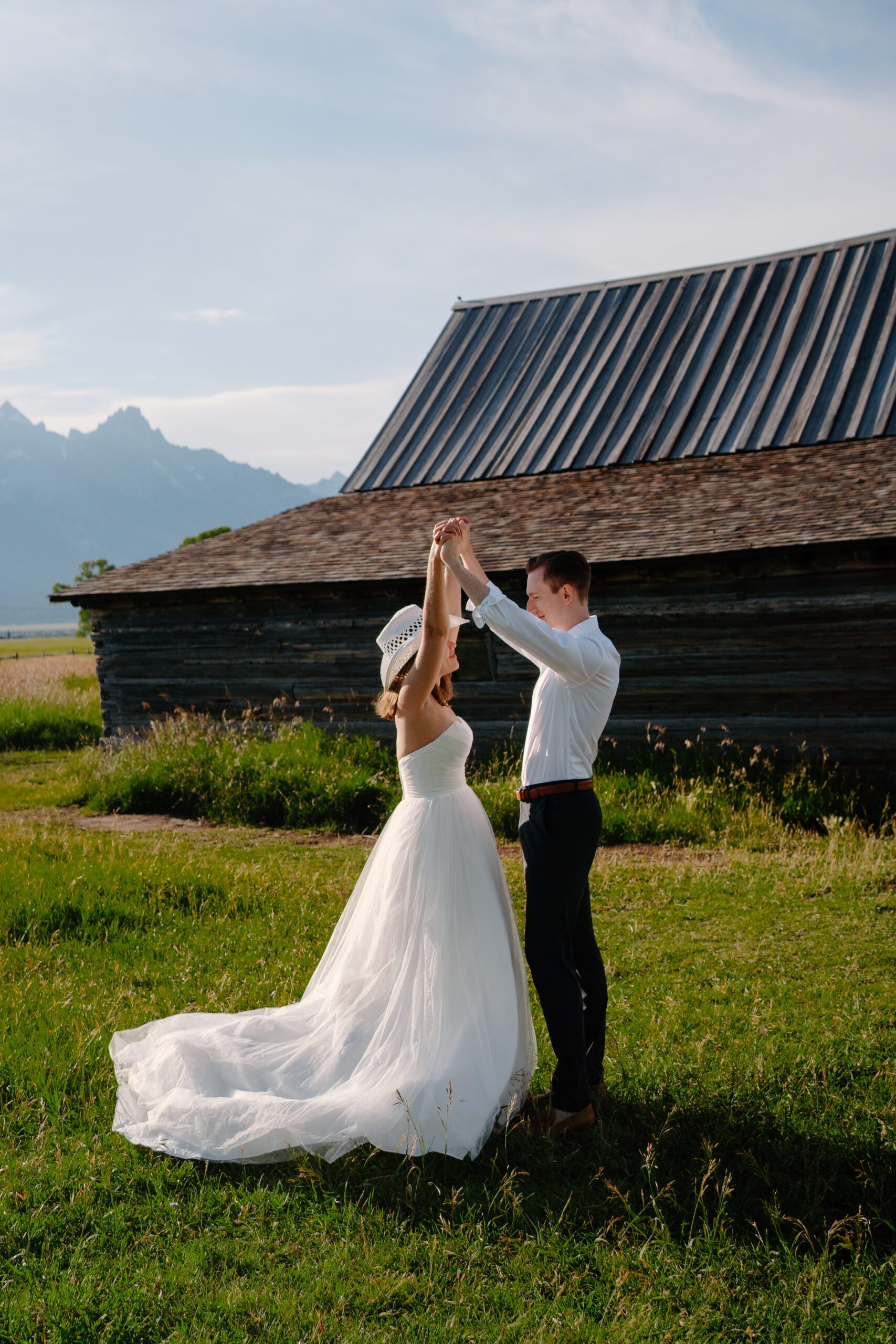 bride and groom holding hands raised above their heads in front of an old barn on mormon row during their grand teton national park elopement