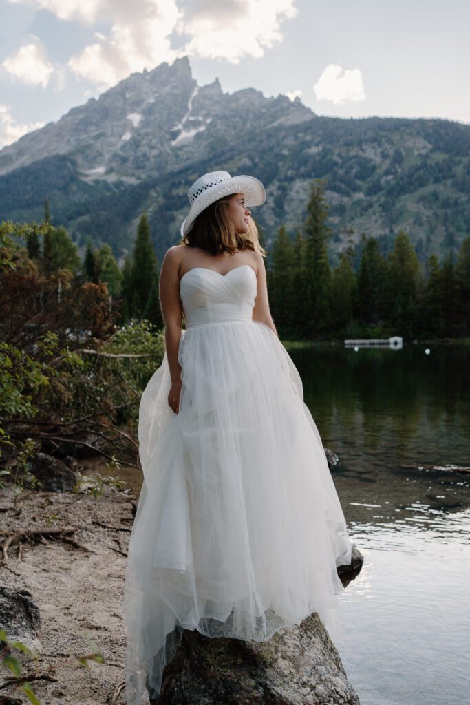 bride standing on a rock at jenny lake in grand teton national park looking at the mountains during her elopement