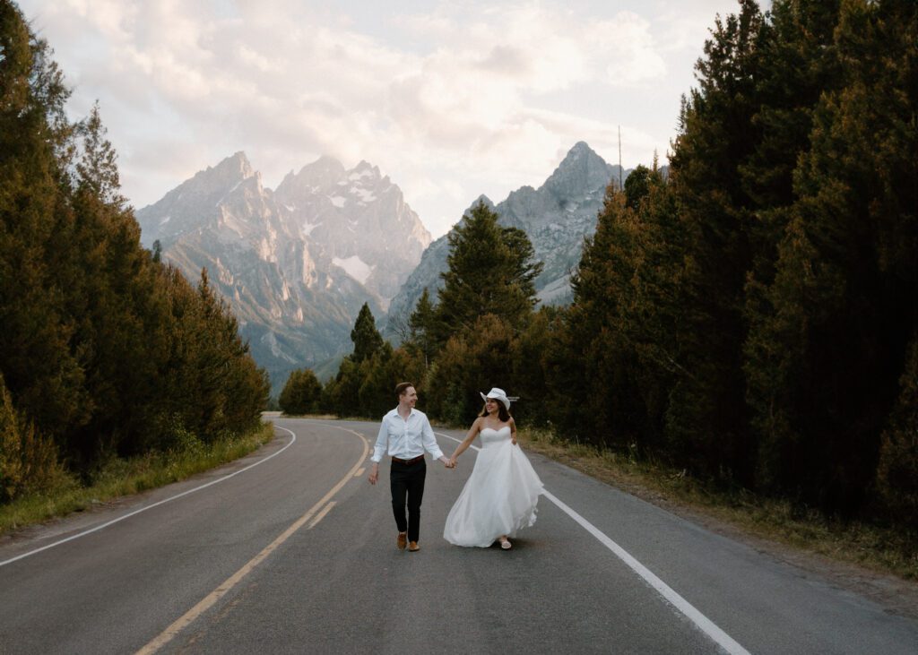 married couple holding hands and running down the road in wedding attire during their grand teton national park elopement