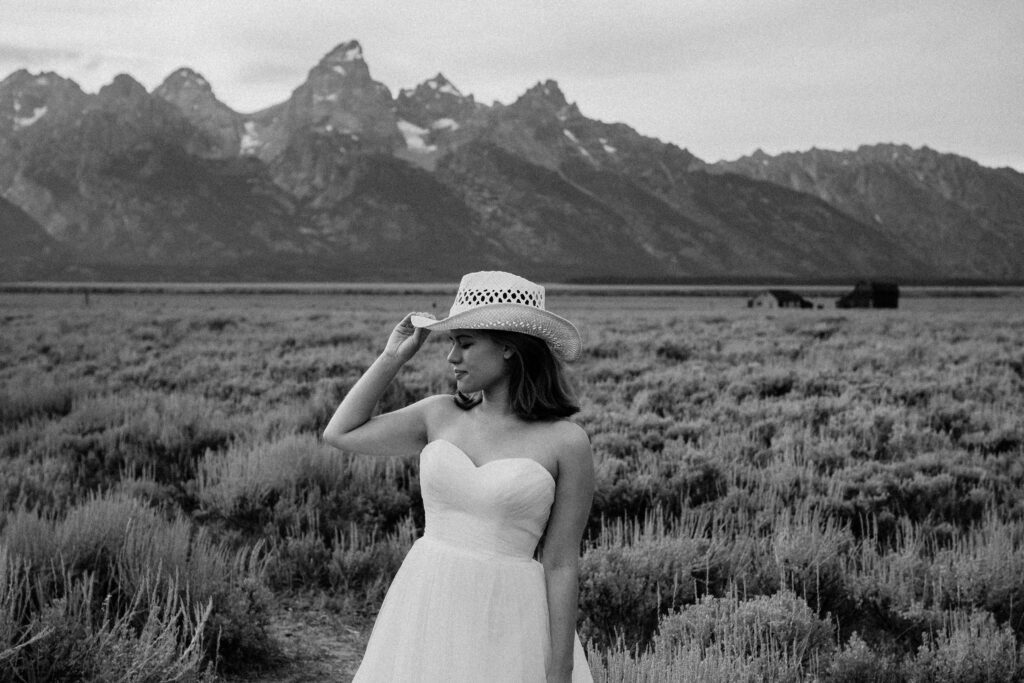 bride wearing a wedding dress and cowboy hat as she looks into the distance of the grand teton mountains during her elopement portraits