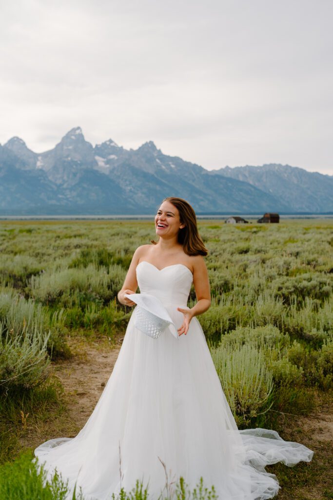 bride in her wedding dress laughing while standing in front of the grand tetons during her elopement