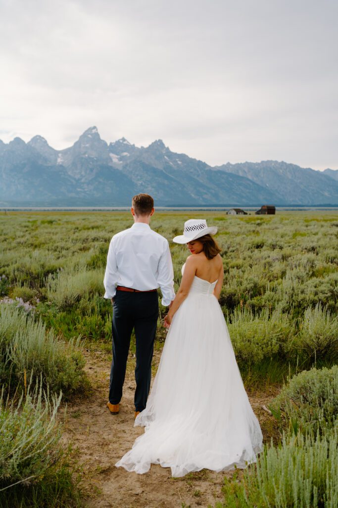bride and groom holding hands in a field at mormon row and looking out at the grand tetons during their elopement