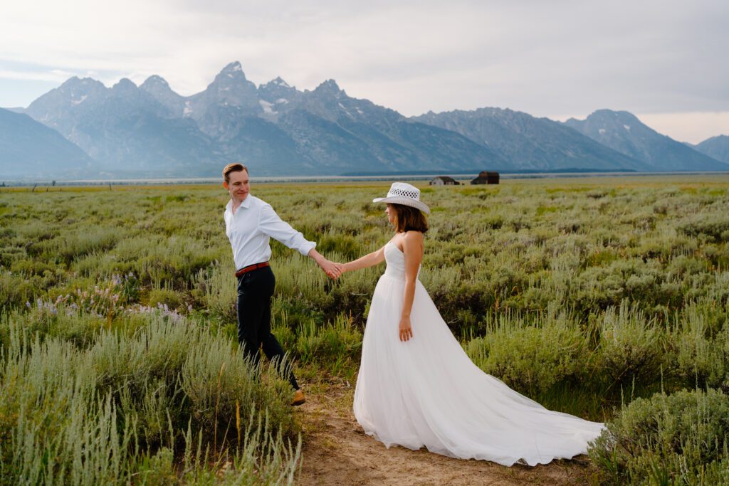 couple walking through a field in wedding attire during their grand teton national park elopement