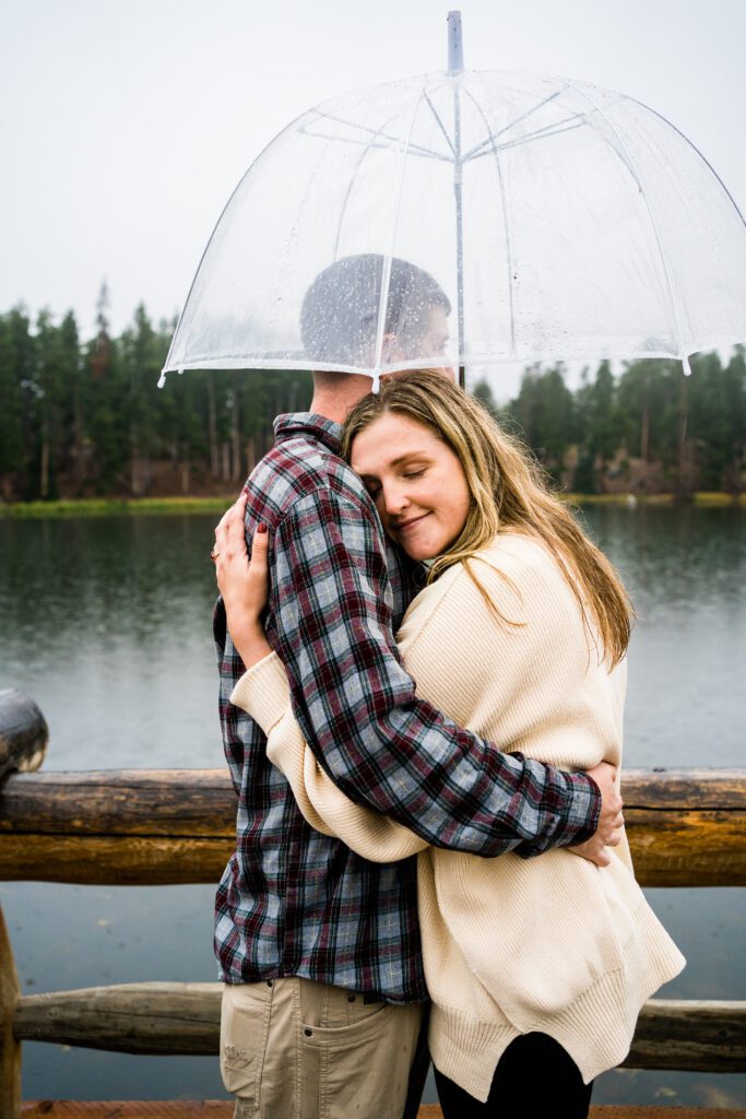 husband and wife hugging eachother with their eyes closed in the rain on the pier at Sprague lake during their rocky mountain national park engagement session