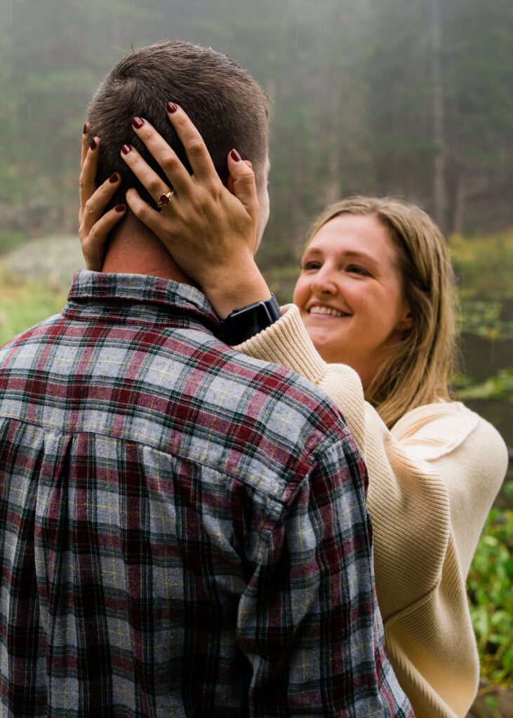 wife holding her husbands head smiling at each other in the forest during their rocky mountain national park engagement session