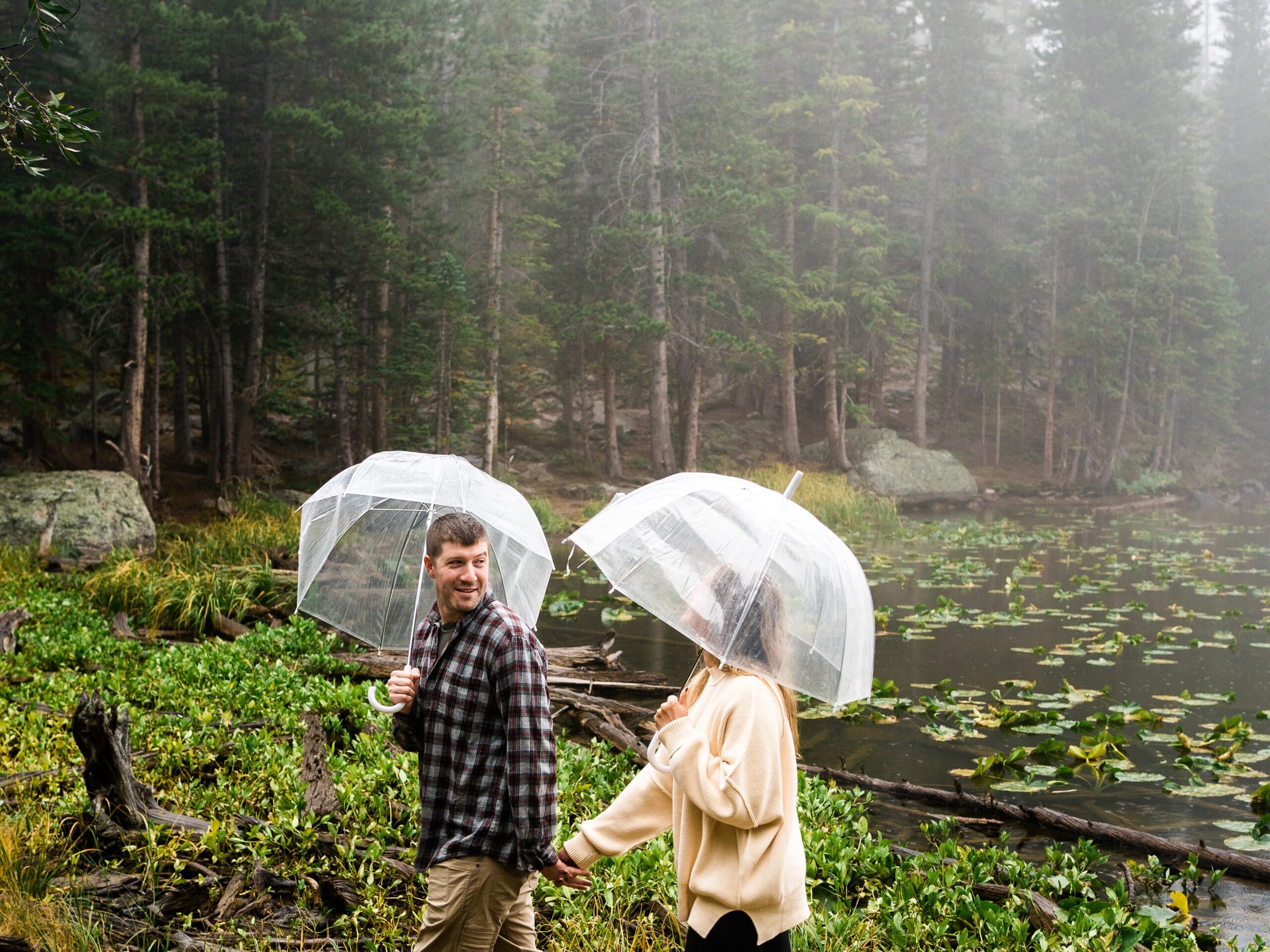 husband and wife holding hands and walking through the forest in the rain during their rocky mountain national park engagement session