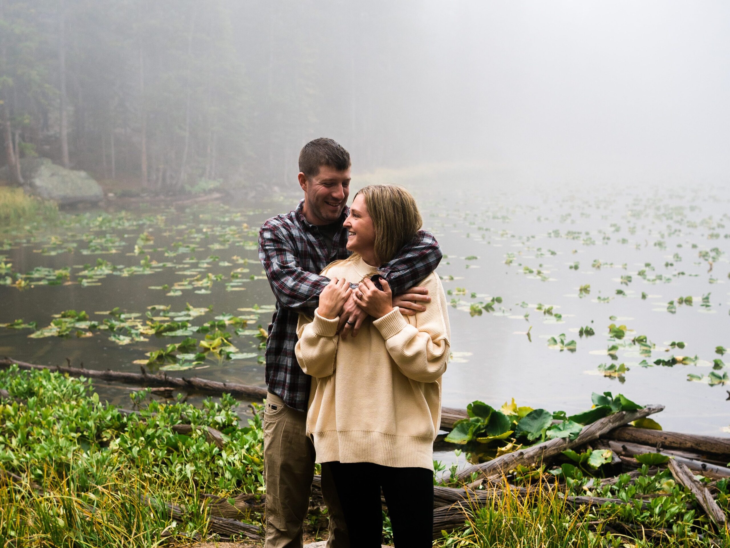 husband hugging his wife from behind in the forest during their rocky mountain national park engagement session