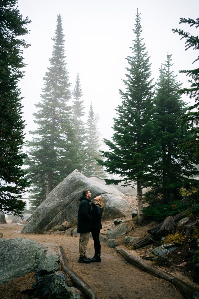 husband and wife holding hands looking up at the sky in the rain during their rocky mountain national park engagement session