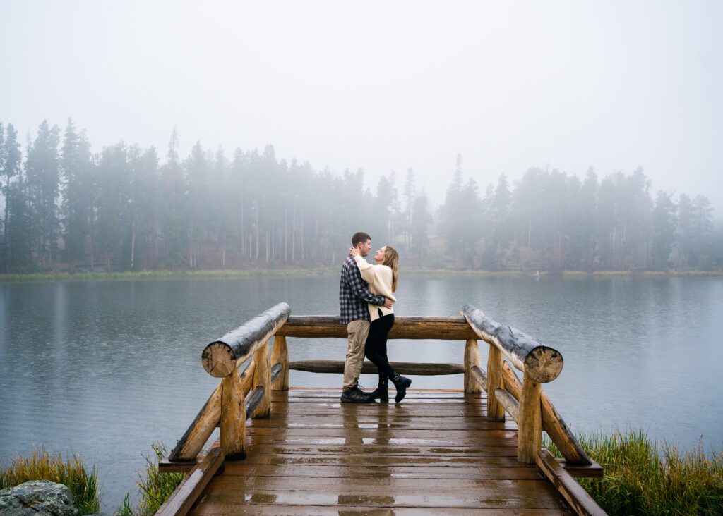 wife hugging her husband around the neck on the pier at Sprague lake during their rocky mountain national park engagement session