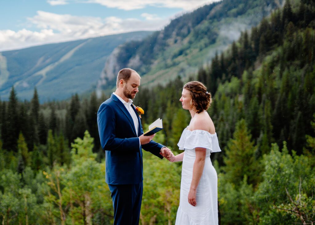 groom holding the brides hand as he reads his marriage vows to her on top of a mountain during their eldora mountain colorado elopement